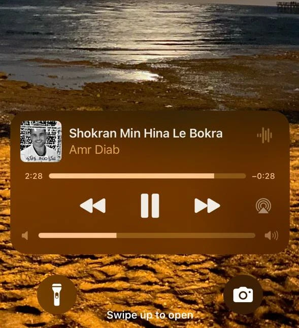 واجهة شاشة القفل في آيفون تُظهر ويدجت تشغيل الموسيقى مع شريط التحكم في الصوت.