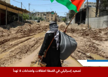 مواطن فلسطيني يرفع علم بلاده وسط طريق موحل دمّره جيش الاحتلال عند مدخل مخيم طولكرم، في مشهد يعكس تصاعد الاعتداءات في الضفة الغربية المحتلة (الفرنسية)