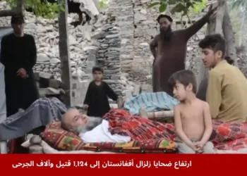 عائلات من ضحايا زلزال أفغانستان تجلس بجوار رجل مصاب ممدد على سرير تقليدي أمام منازل مدمرة في ولاية كونار بعد الكارثة.