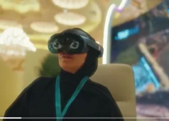 امرأة سعودية ترتدي نظارة واقع افتراضي ثلاثية الأبعاد خلال مؤتمر دولي في الرياض يناقش استدامة الإنترنت، مع خلفية رقمية مضيئة توضح خرائط وتقنيات حديثة.