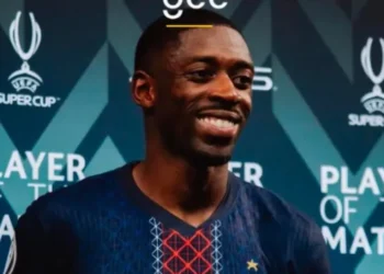 عثمان ديمبيلي لاعب باريس سان جيرمان يحتفل بعد فوزه بجائزة أفضل لاعب في مباراة كأس السوبر الفرنسي، مرتديًا قميص الفريق أمام خلفية شعار البطولة