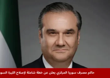 حاكم مصرف سوريا المركزي خلال إعلانه عن خطة إصلاح شاملة لليرة السورية، يظهر بجانبه علم سوريا، في سياق الإصلاح النقدي لليرة السورية.